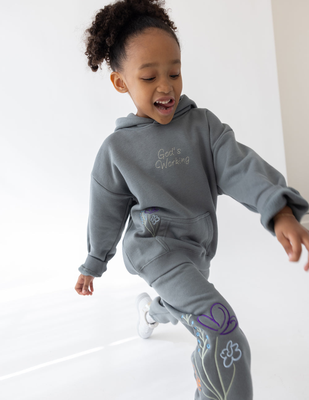 Kids wearing oversized God's Still Working hoodies in Sedona Sage with embroidered Psalm 138:8 design