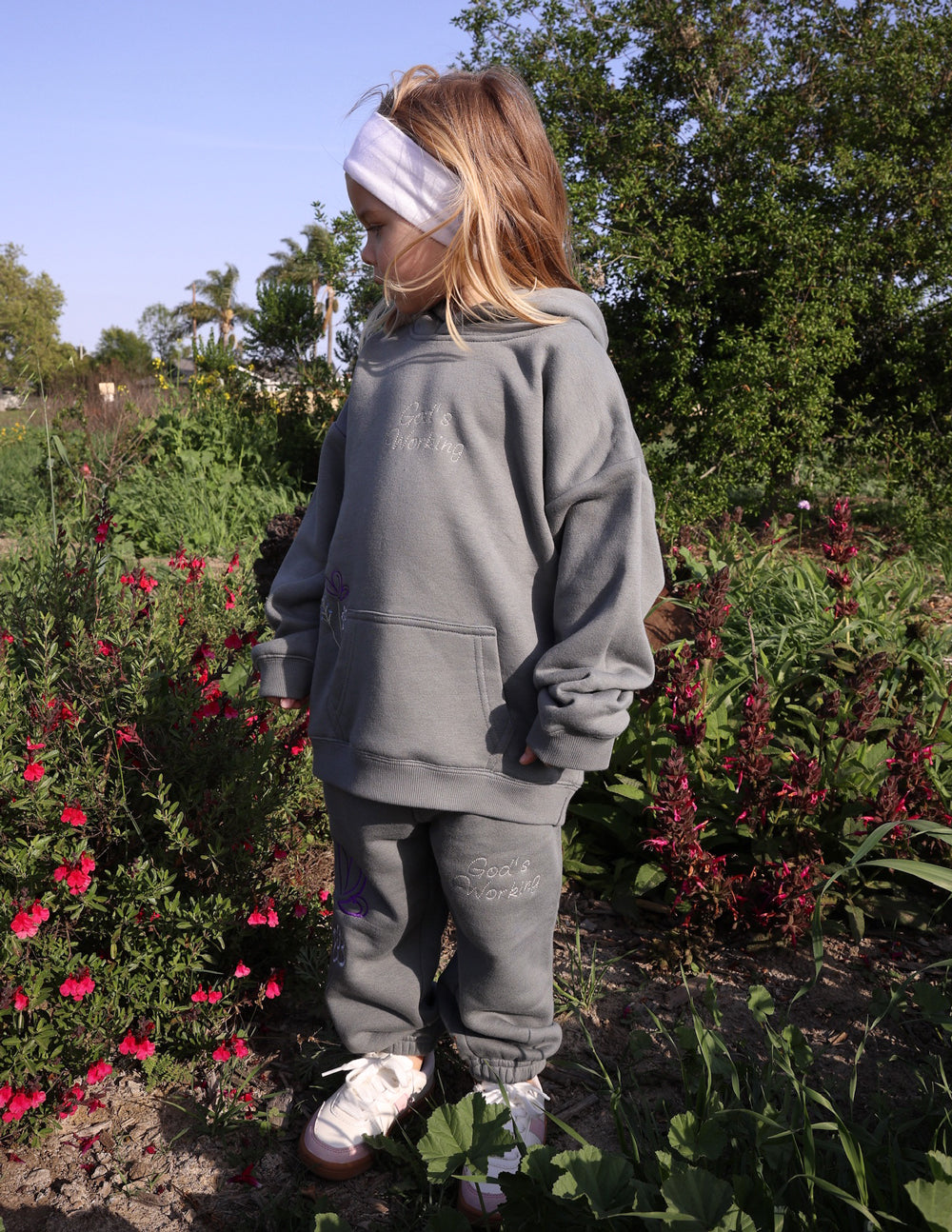 Kids wearing God's Still Working hoodie in oversized Sedona Sage design with Psalm 138:8 embroidery
