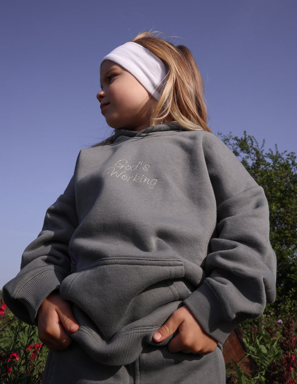 Child wearing God's Still Working Kids Hoodie in Sedona Sage with oversized fit and embroidered Psalm 138:8 design